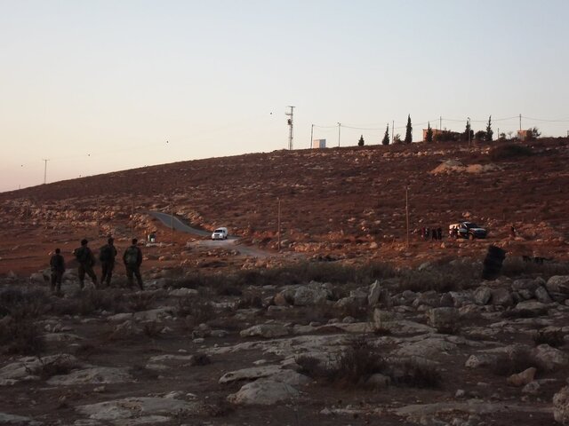 Soldiers standing while police talks to settlers
